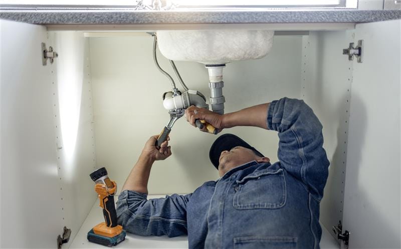 Plumber repairing pipes beneath a bathroom sink in Greenacres
