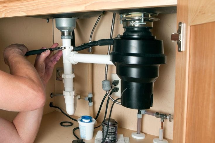 Plumber installing a garbage disposal beneath a kitchen sink in Greenacres