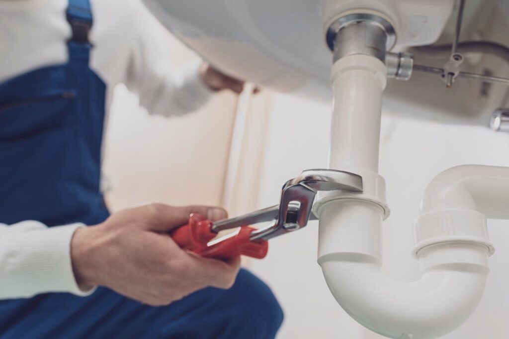 Plumber repairing a white drain pipe beneath a sink in Greenacres