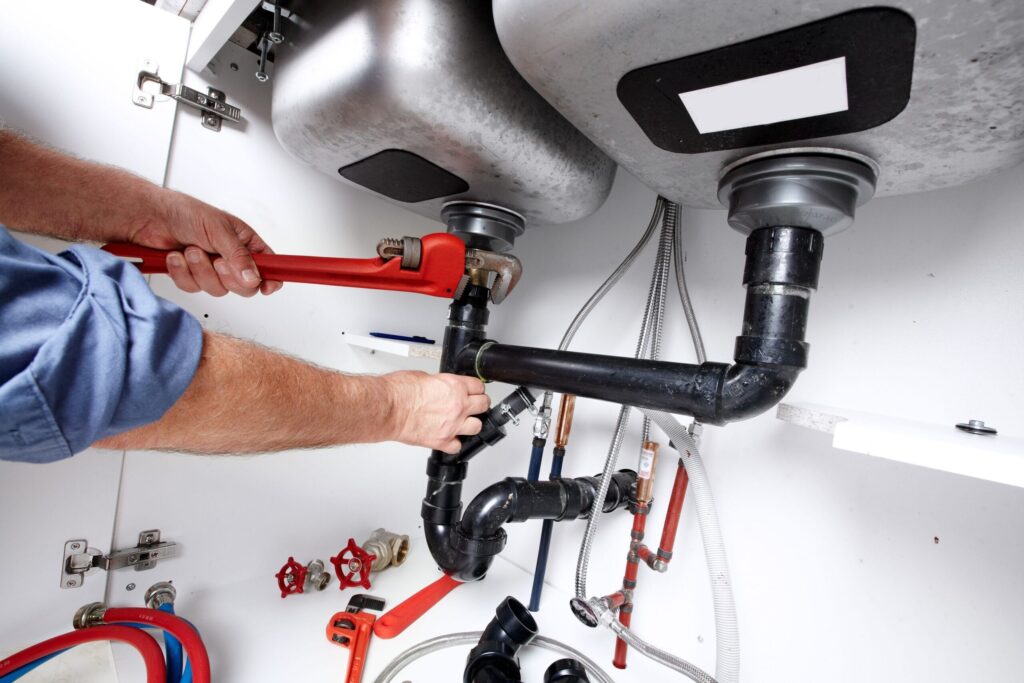 Plumber repairing drain pipes beneath a kitchen sink in Greenacres
